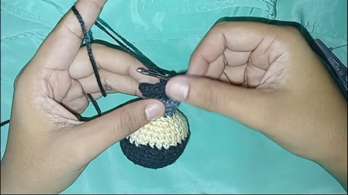 Hands working a black and tan color change section on a Batman amigurumi head in progress with a silver hook.