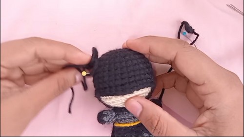 Hands attaching a crocheted ear point to the black head of a Batman amigurumi with a gold pin holding it in position.
