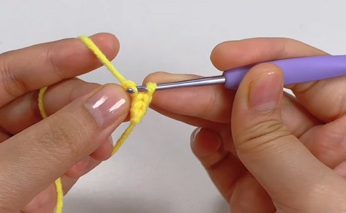 Close-up of hands using a purple crochet hook to work the first few stitches of a magic ring in yellow yarn for a bee amigurumi.