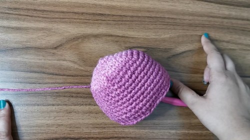 Crocheted purple round cat head piece with a yarn tail resting on a wooden surface showing a completed head before assembly