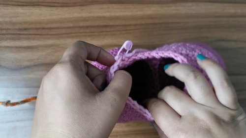 Hands stuffing a crocheted purple heart shaped cat body with fiberfill using a pink crochet hook to push filling inside