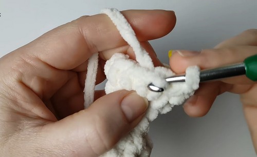 Hands using a green crochet hook to work white chenille yarn stitches through the beginning rounds of a small goose body piece.