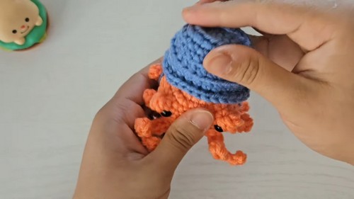 Hands fitting the blue crocheted bucket shell over the orange hermit crab amigurumi body to check the sizing and fit.