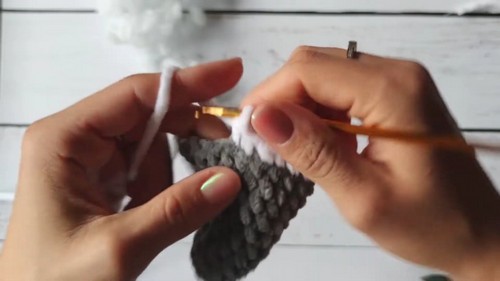 Hands crocheting a gray and white color change section of a bear body using a gold hook showing the sweater transition row