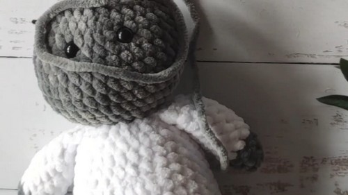 Side view of a crochet bear amigurumi body with the head tilted forward showing gray and white chenille texture before final assembly