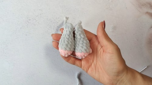 Hand holding two small crocheted gray elephant legs with pink bottoms showing the finished leg pieces before assembly