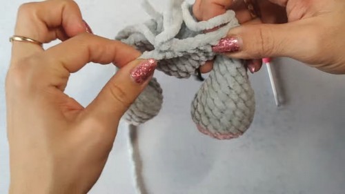 Two hands joining the body parts of a gray and pink crochet elephant amigurumi together with yarn tails visible