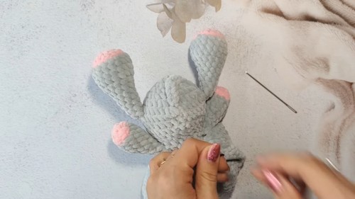 Back view of a gray crochet elephant amigurumi being held showing pink tipped legs and arms before the head is attached