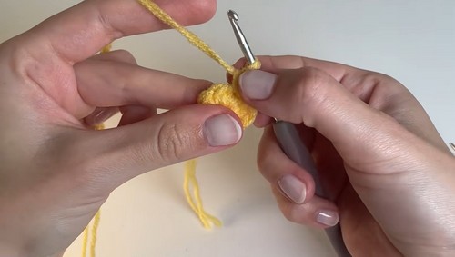 Hands beginning a yellow crochet piece from a foundation chain with a gray hook, yarn tail hanging loose.
