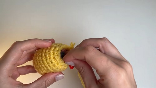 Hands closing and stuffing a yellow crochet Easter egg with a red stitch marker visible at the opening.