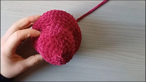 Hand holding a large crocheted dark red oval shaped dragon body piece with a yarn tail showing work in progress