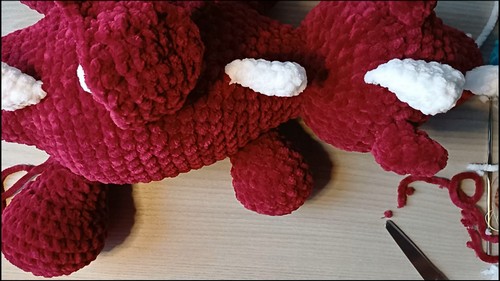Close up of a large crochet baby dragon amigurumi body showing white spike details along the back with a crochet hook resting nearby