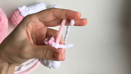 Hand holding two slim crocheted pink and white cow legs joined at the top with a stitch marker