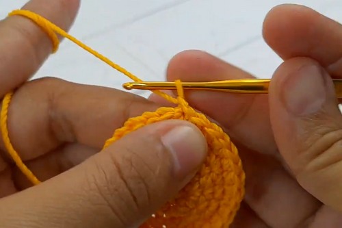Hands crocheting orange rounds of a tiger ball body with a gold hook.