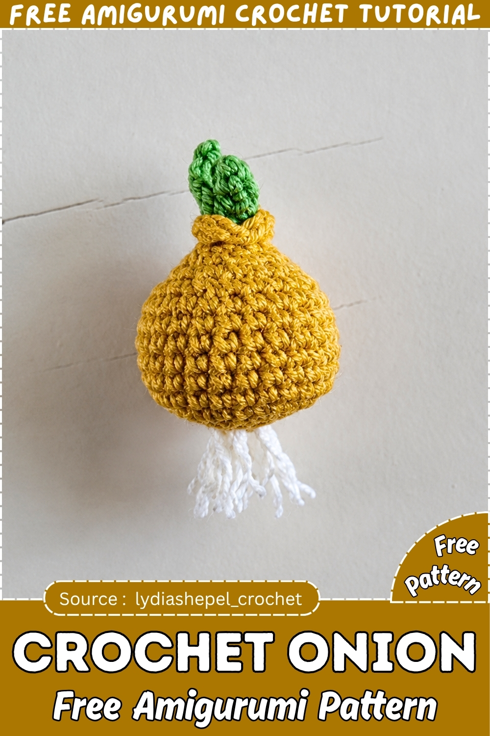 Completed crochet onion amigurumi in golden yellow yarn with a compact green sprout top and loose white yarn roots at the bottom, photographed flat against a white textured wall.
