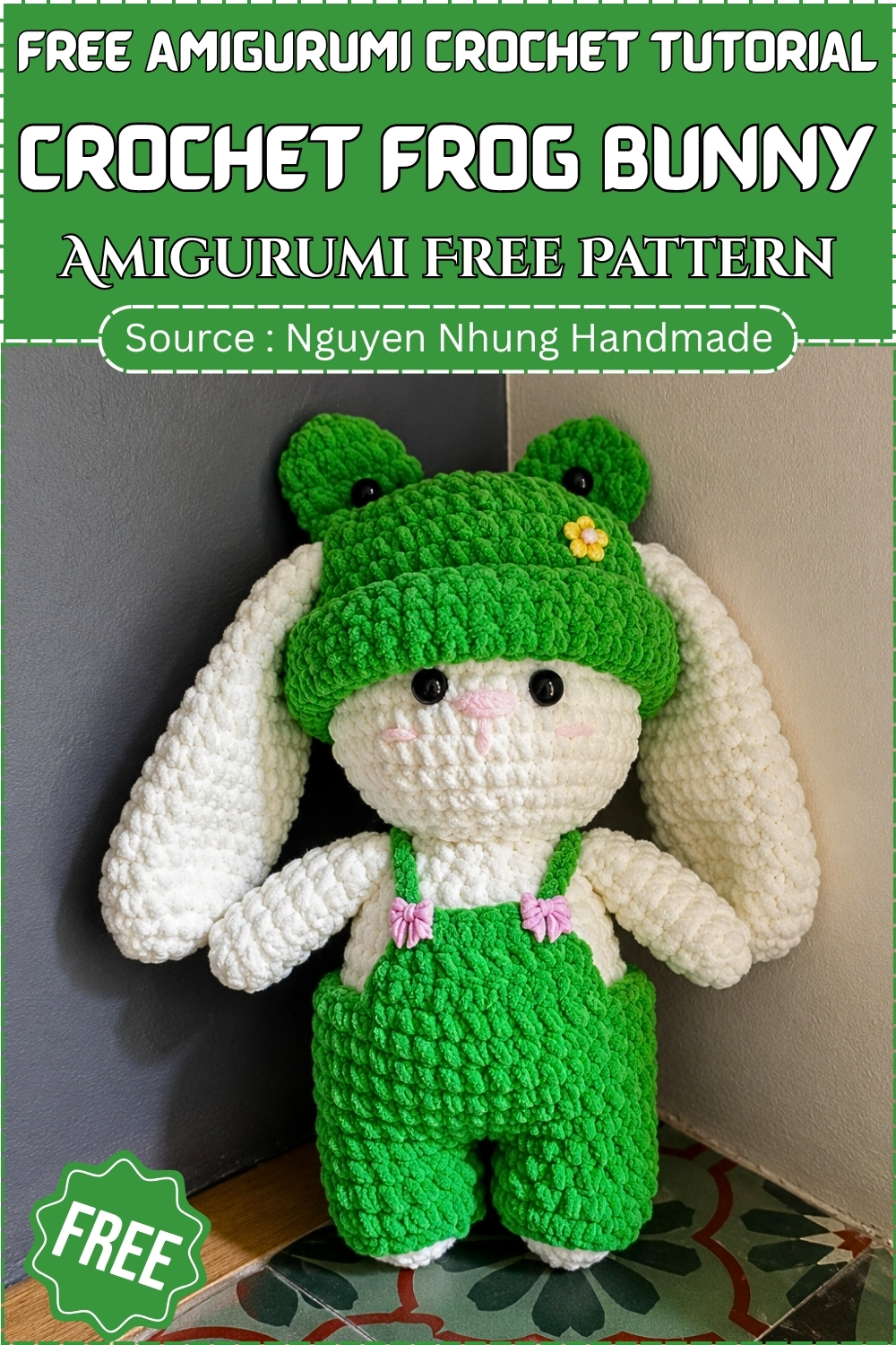Completed crochet frog bunny amigurumi in white chenille with oversized floppy ears, a bright green frog hat, and matching green dungarees with pink bow closures, posed upright in a corner.