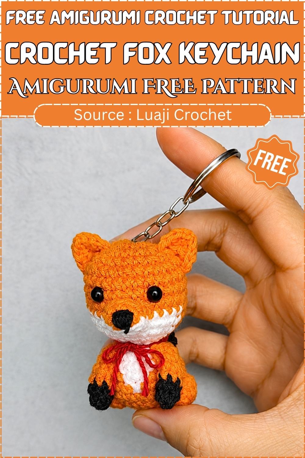 Finished crochet fox keychain amigurumi in orange white and black with a red ribbon bow held up in a hand against a light gray background