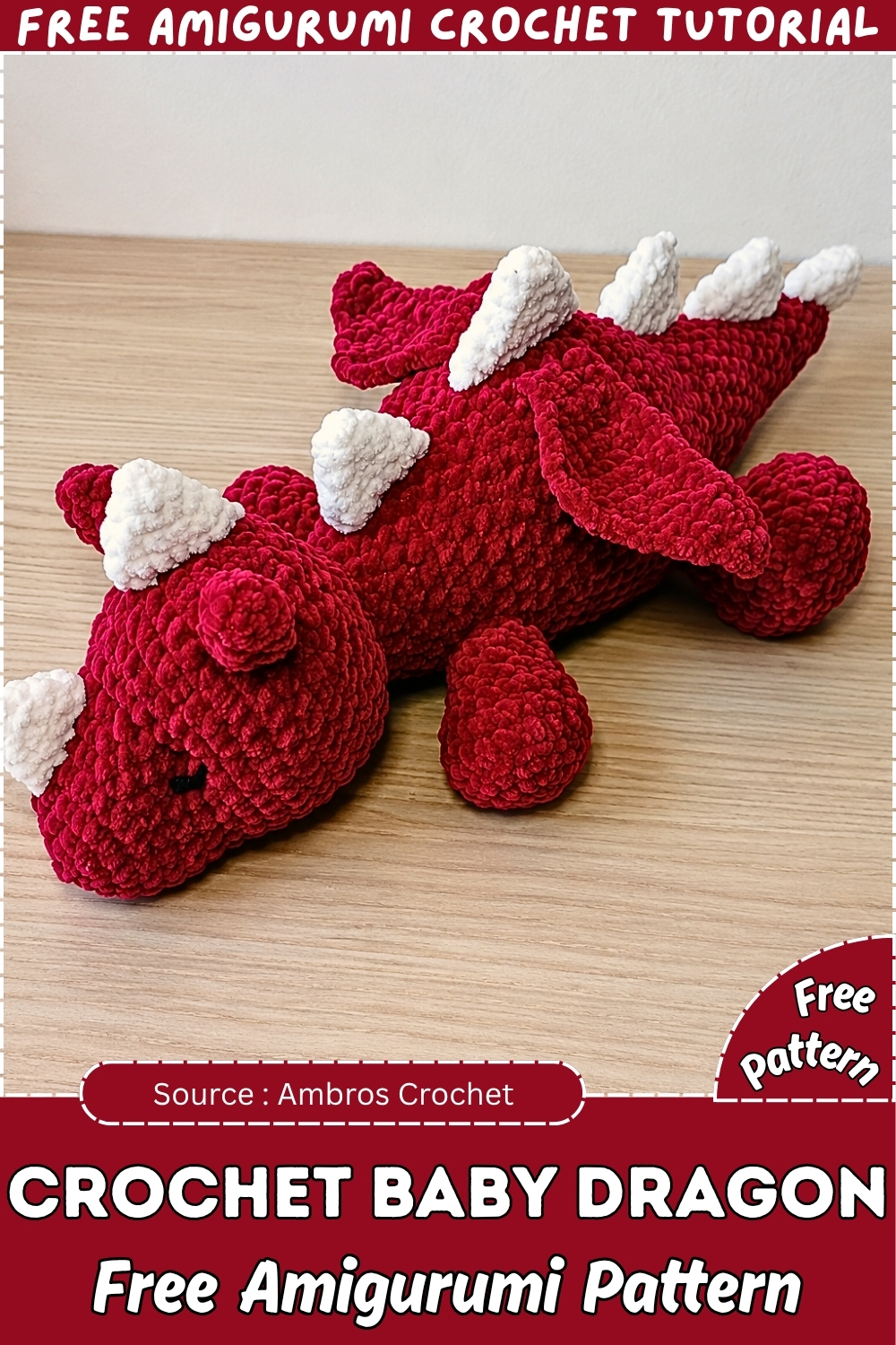 Completed crochet baby dragon amigurumi in dark red chenille with white spines wings and tiny horns displayed on a wooden table