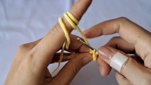 Yellow yarn looped around a finger while starting the magic ring for a crochet baby chick.