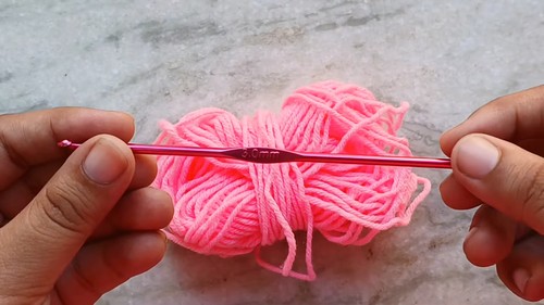 Hands holding a small ball of bright pink yarn with a pink crochet hook showing the materials used for the mini heart