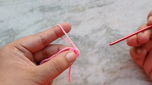 Hands forming a magic ring with pink yarn and a red crochet hook as the starting step of the mini heart pattern