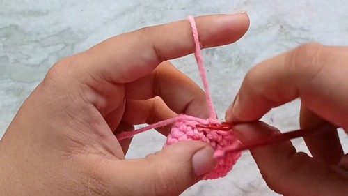 Hands joining two crocheted pink heart halves together with yarn showing the construction process up close