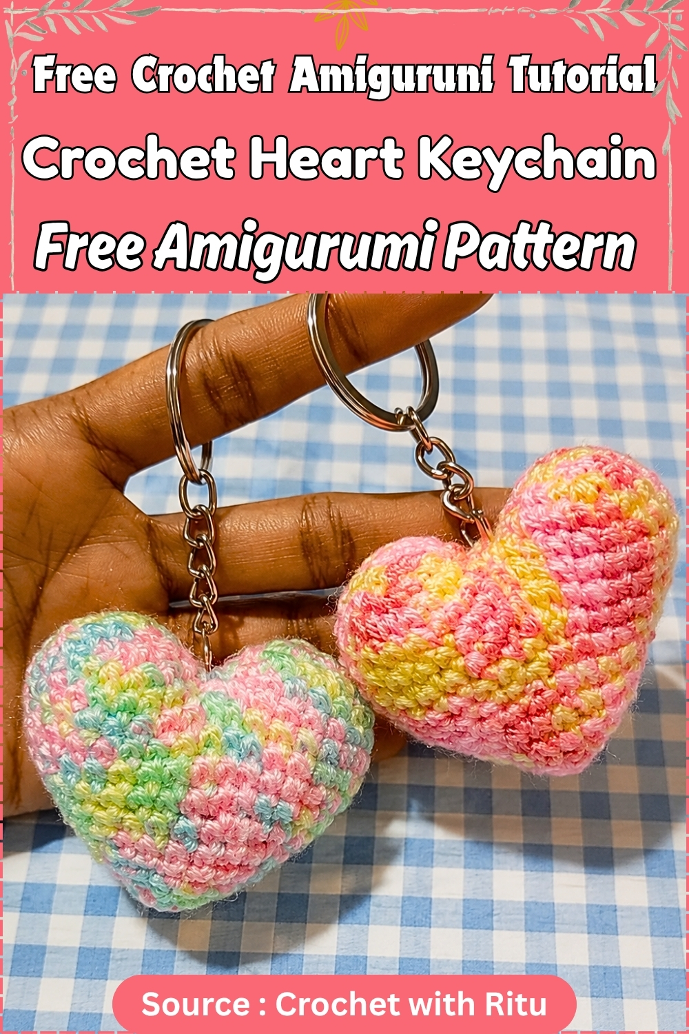 Two completed pastel variegated crochet heart keychains with silver rings and chains held in a hand against a blue gingham background, one in pink and yellow and one in rainbow tones.