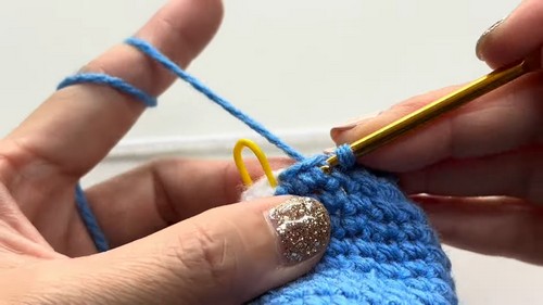 Close-up of hands working blue yarn onto a yellow crochet hook while crocheting a whale shark amigurumi body.