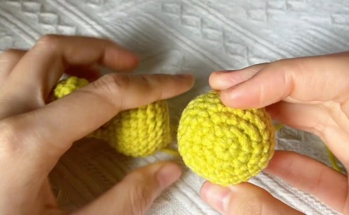 A rounded yellow crocheted head piece held between fingers beside other chameleon parts.