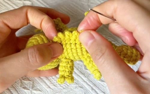 Shaping the legs of a yellow one piece crochet chameleon with a hook and yarn.