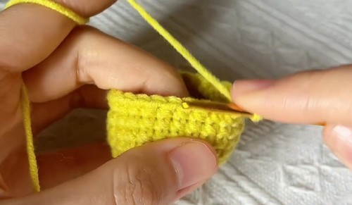 Hands working a row of stitches along a flat yellow crochet piece for a one piece chameleon.