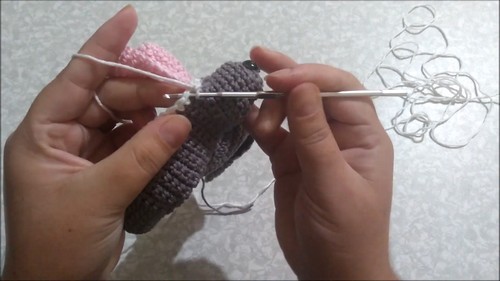 Hands using a tapestry needle to sew a pink piece onto a gray crochet hammerhead shark amigurumi in progress.