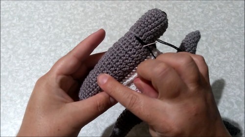 Hands attaching the distinctive wide hammer-shaped head to a gray crochet hammerhead shark amigurumi body.