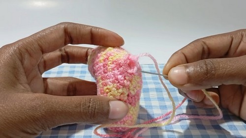 Hands closing the top opening of a small stuffed pastel crocheted heart using a tapestry needle and yarn tail.