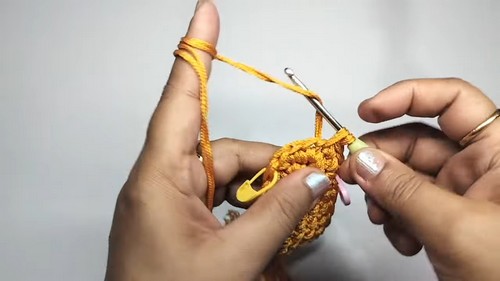 Hands using a pink crochet hook and yellow stitch marker to work the beginning rounds of a small golden yellow giraffe head piece.
