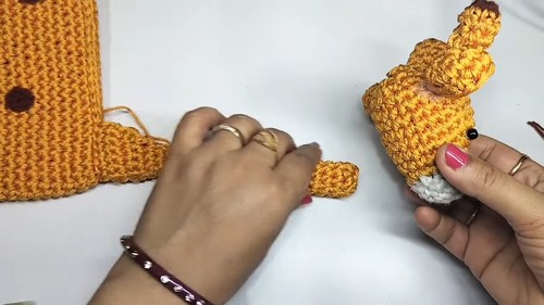 Hands holding the flat yellow giraffe bag body alongside the finished amigurumi giraffe head piece, showing the two main components before final joining.