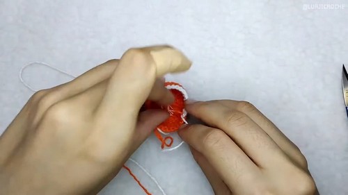 Hands joining two small crocheted orange and white fox face pieces together showing the muzzle construction step