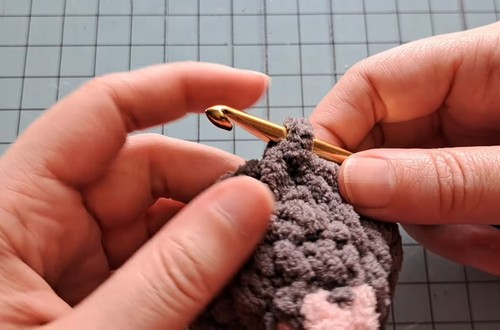 Hands working early dark gray chenille rounds with a gold hook on a grid cutting mat.