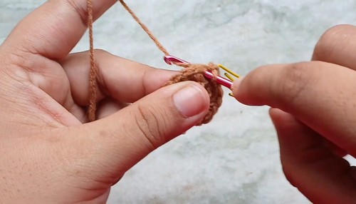 Hands crocheting into a small brown magic ring with colorful stitch markers holding the round open showing an early body piece in progress