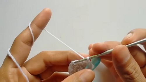 Close-up of hands using a silver crochet hook to work the first few stitches of a small white yarn piece for a fluffy owl amigurumi.