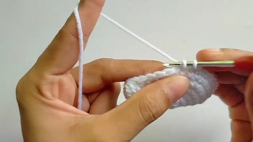 Hands working a chain row in white yarn with a silver crochet hook showing an early construction step for the owl pattern