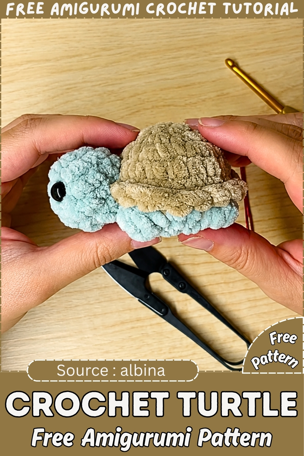 Two hands holding a finished crochet turtle amigurumi with a light blue chenille body and tan chenille shell, displayed on a branded free pattern tutorial graphic with scissors and a gold hook visible on the wood surface.