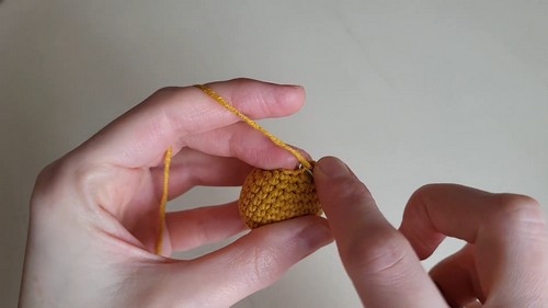 Hands working the decreasing rounds of a golden yellow crocheted onion body, showing the tapered neck shape forming near the top.