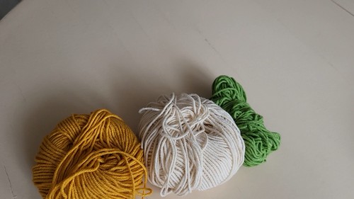Three balls of yarn in golden yellow, white, and green laid on a white surface, showing the materials needed for a crochet onion amigurumi.