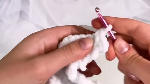 Close-up of hands crocheting white velvet yarn with a pink hook, forming the belly section of a shark amigurumi.