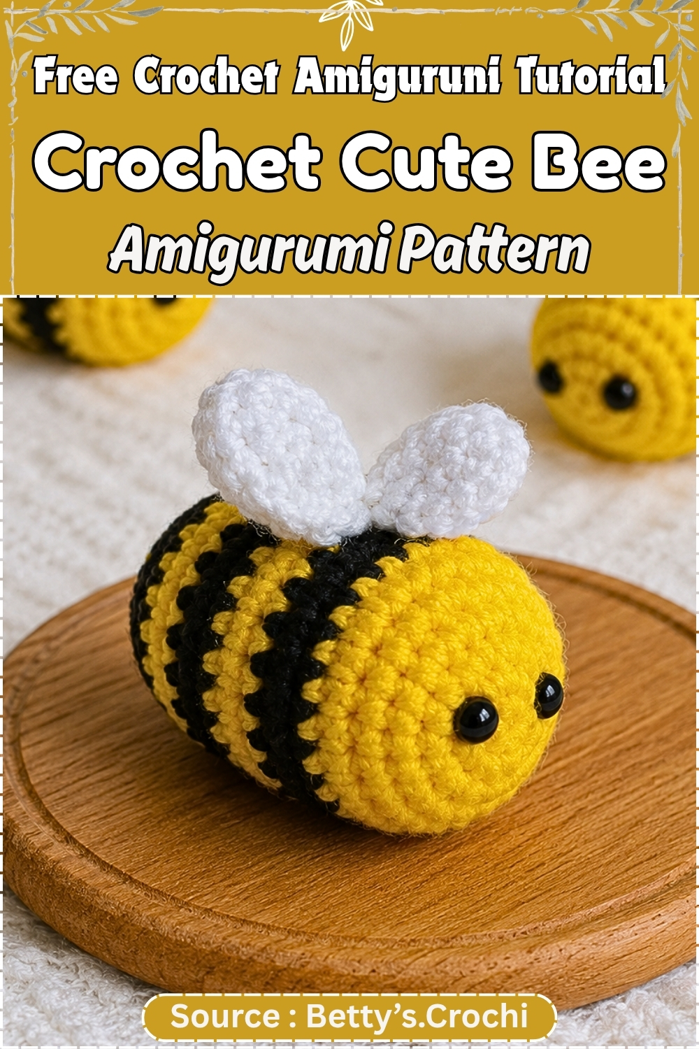 Finished yellow and black striped crochet bee amigurumi with white wings and black bead eyes displayed on a small wooden board, with additional bees blurred in the background.